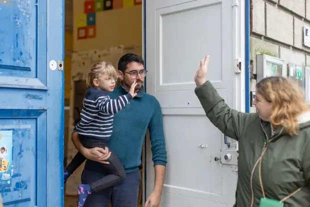Photo d'un intervenant avec un jeune enfant dans les bras disant aurevoir avec la main à un parent